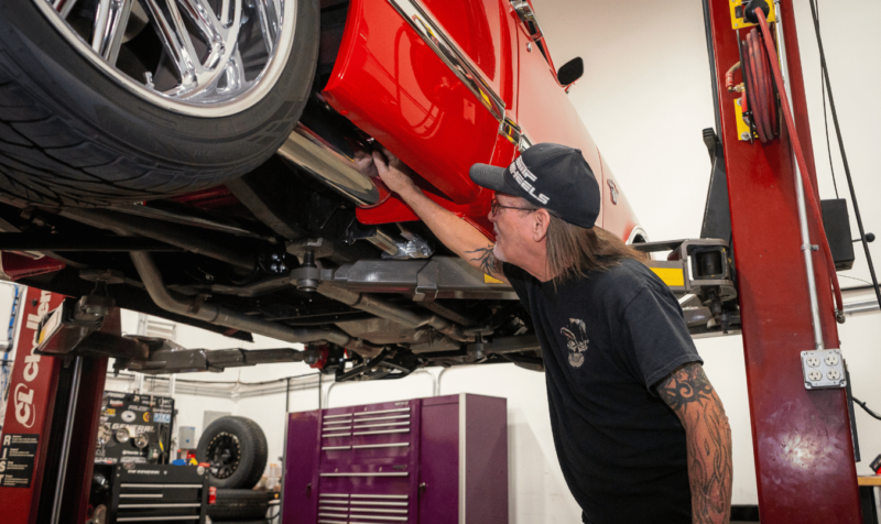 The Custom Shop LV technician working beneath a red custom vehicle on a lift