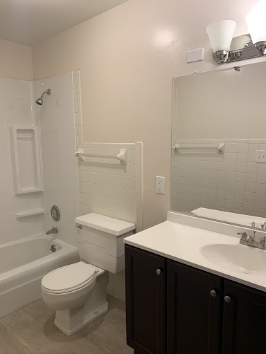 Renovated apartment bathroom with a white tub, toilet, and dark vanity