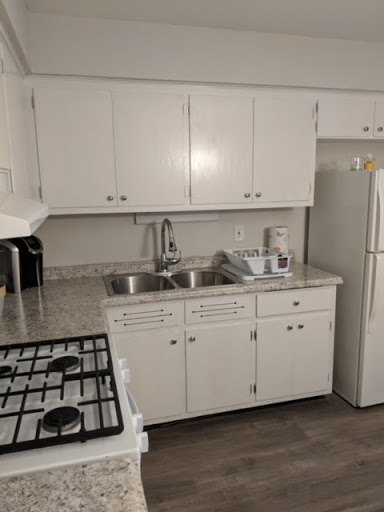 Renovated apartment kitchen with white cabinets, speckled countertops, and wood-look flooring