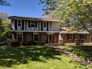 Updated front exterior with brown shutters, a lawn, and mature trees