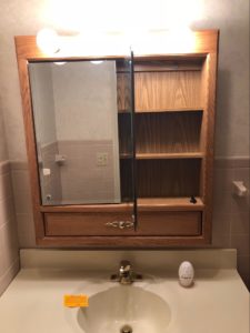 Bathroom before renovation with a wood medicine cabinet and dated light fixture