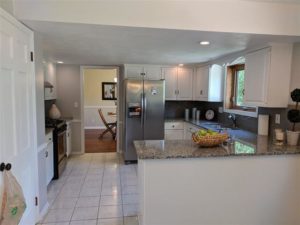 Renovated kitchen with granite countertops, white cabinets, and a stainless steel refrigerator