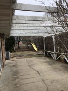 Back patio before renovation with an aging overhead trellis and a swing set