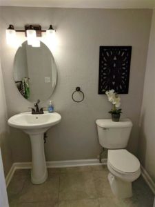 Renovated powder bathroom with a pedestal sink, oval mirror, and updated lighting